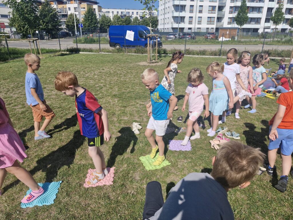 Dzieci pokonują na trawie ścieżkę sensoryczną. 