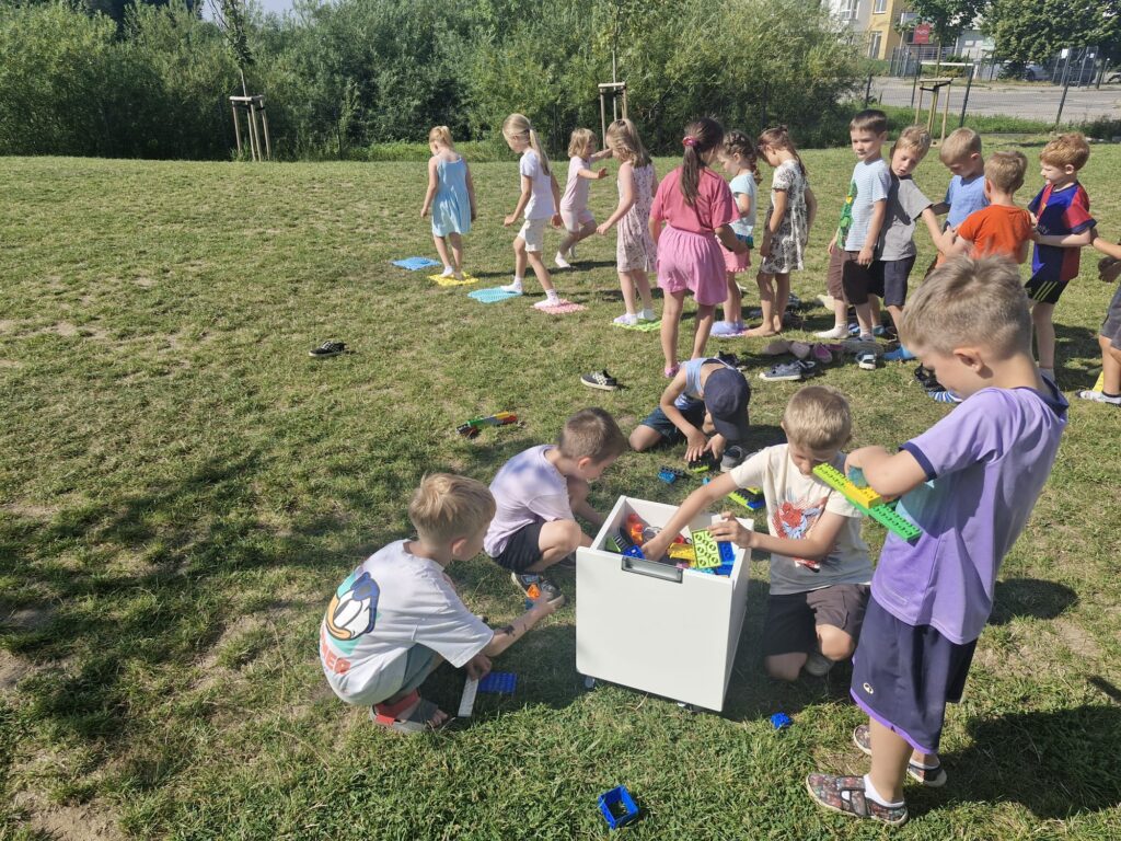 Dzieci na trawie budują z klocków i pokonują ścieżkę sensoryczną. 