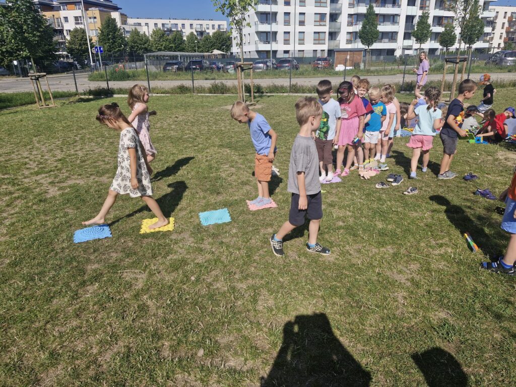 Dzieci pokonują na trawie ścieżkę sensoryczną. 